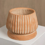 Terracotta-colored ceramic pot with ribbed texture on a white surface.