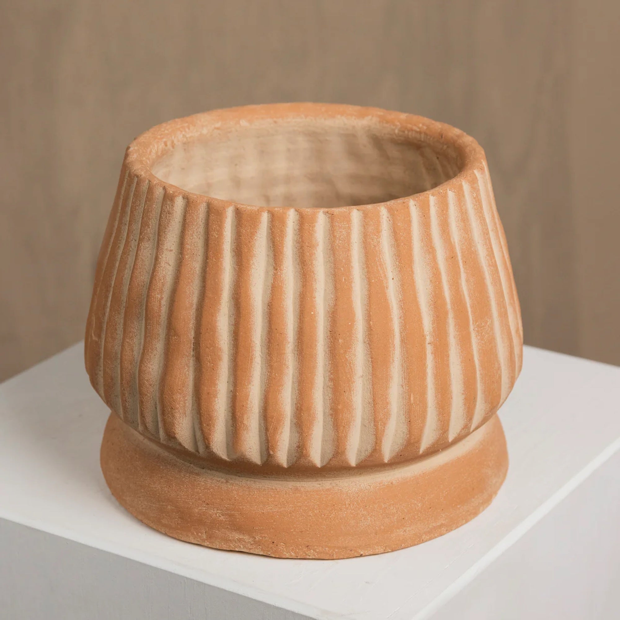 Terracotta-colored ceramic pot with ribbed texture on a white surface.