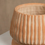Terracotta-colored ceramic pot with ribbed texture on a white surface.
