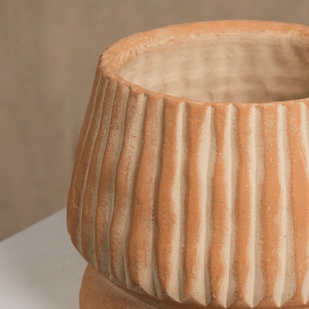 Terracotta-colored ceramic pot with ribbed texture on a white surface.
